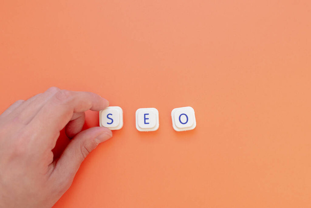 A hand is placing the letter "S" to form the acronym "SEO", for Search engine optimization, over an orange background. Web search engines and its importance concepts - Photo, Image