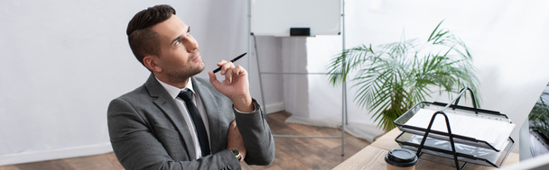 вдумчивый трейдер держит ручку и смотрит на рабочее место в офисе, баннер - Фото, изображение
