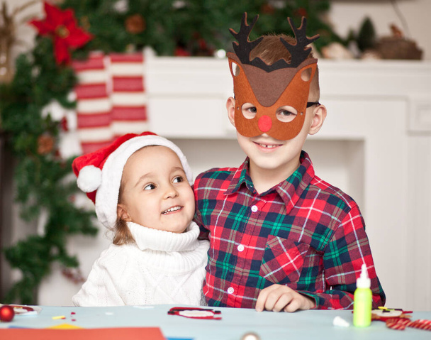 Fanny kids girl and boy in Santa cap and deer mask congratulate each other Merry Christmas and Happy New Year and hug. - Foto, immagini