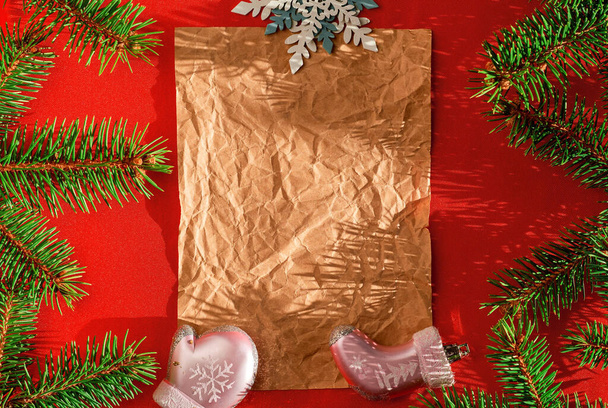Festliche Weihnachtskarte mit Tannenzweigen und festlichem Schmuck auf rotem Hintergrund. Weihnachtsvorlage für Banner oder Wunschzettel. Draufsicht, Layout, helles Sonnenlicht auf Vintage-Papier - Foto, Bild