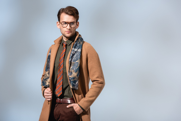 stylish man in glasses and winter coat standing with hand in pocket on grey - Photo, Image