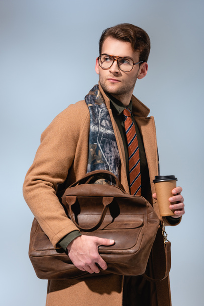 stylish man in winter coat holding paper cup and leather briefcase on grey  - Photo, Image
