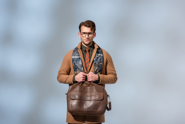 stylish man in winter coat holding brown briefcase on grey  - Фото, изображение