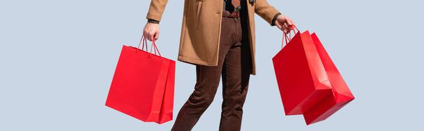 partial view of customer in coat holding paper bags isolated on grey, banner - Fotoğraf, Görsel