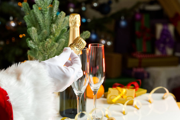 man in santa claus costume opens a bottle of champagne - Photo, Image