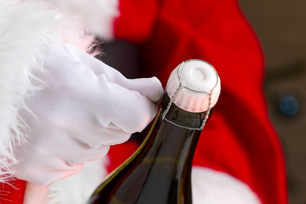 man in santa claus costume opens a bottle of champagne - Photo, Image