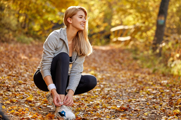 young runner woman tying laces for autumn run in forest park - Foto, Bild