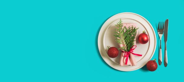 Website banner with served plate and cutlery for celebration of Christmas and New Year. On plate is a napkin with Christmas tree branch, red balls. Flatlay banner on bright blue background. Top view - Foto, Imagen