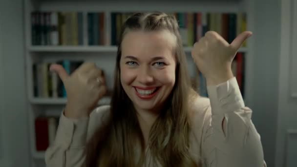 Portret wesołej białej damy pokazujący kciuk w górę na dwóch ruchomych dłoniach siedzących w pokoju - Materiał filmowy, wideo