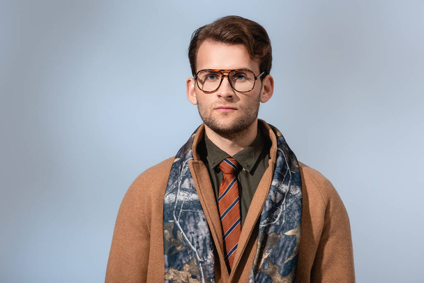 trendy man in glasses and winter coat looking at camera on grey - Foto, afbeelding