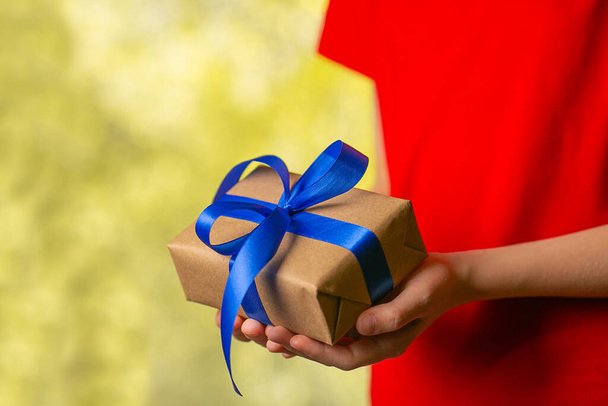 Hände halten Craft-Geschenkbox mit blauem Band auf abstraktem Bokeh-Hintergrund. - Foto, Bild