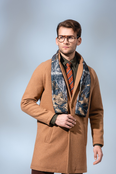 trendy man in glasses, scarf and winter coat looking away on grey - Фото, изображение