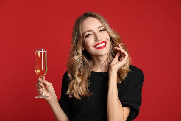 Happy young woman with glass of champagne on red background. Christmas celebration - Фото, изображение