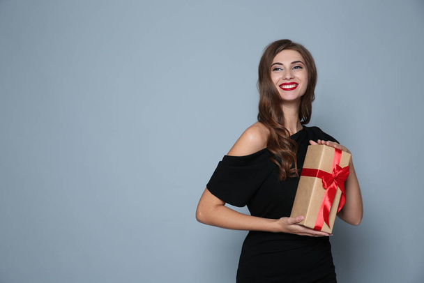 Happy woman with gift box on grey background, space for text. Christmas party - Photo, Image