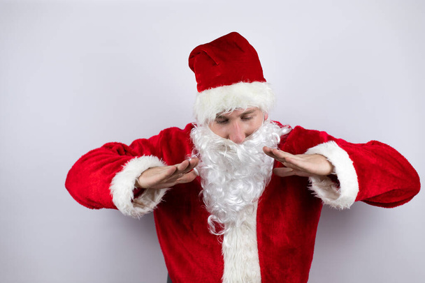 Als Weihnachtsmann verkleideter Mann steht vor isoliertem weißen Hintergrund und schreit laut mit den Händen auf dem Mund nach unten - Foto, Bild