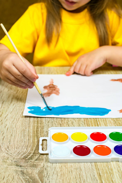 Primo piano di una mano di bambini con un disegno di spazzola e acquerelli. Artista per bambini disegna, creatività, ricreazione, formazione, disegno, corsi di colore, pittura, studi di colore. Una ragazzina con una T gialla - Foto, immagini