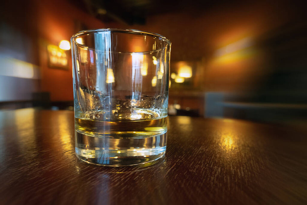 Juon viskiä tyhjässä baarissa. Kultainen värillinen alkoholijuoma puupöydällä pubissa. Rentoutuminen töiden jälkeen, viinan juominen - Valokuva, kuva