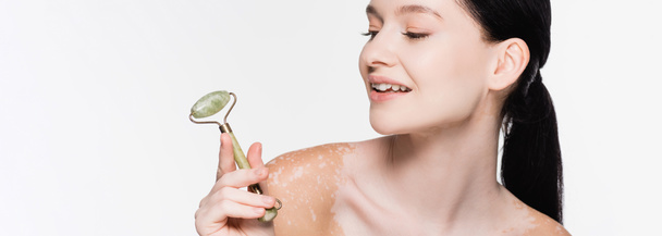 sorrindo jovem mulher bonita com vitiligo segurando rolo de jade no rosto isolado no branco, banner - Foto, Imagem