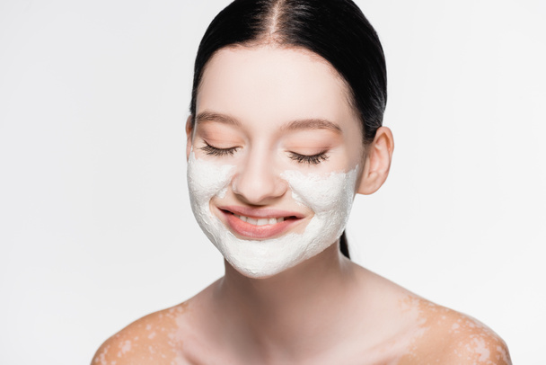 χαμογελαστή νεαρή όμορφη γυναίκα με λεύκη και πήλινη μάσκα στο πρόσωπο απομονωμένη σε λευκό - Φωτογραφία, εικόνα