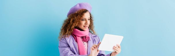 young woman in winter coat, beret and pink knitted scarf holding digital tablet on blue, banner - Fotografie, Obrázek