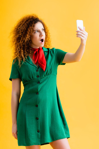 shocked young woman in green dress taking selfie on yellow  - Foto, Imagen