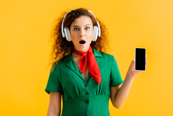 cheerful woman in wireless headphones holding smartphone with blank screen isolated on yellow  - Foto, immagini