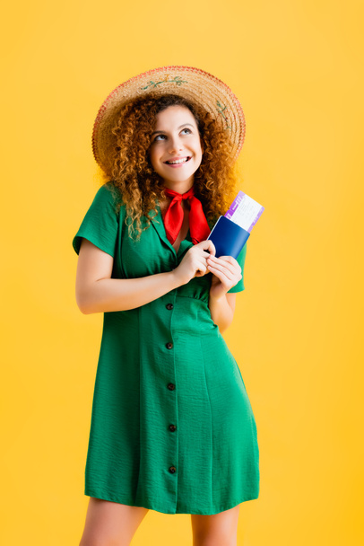 mujer feliz en sombrero de paja con pasaporte con billete de remo aislado en amarillo  - Foto, Imagen
