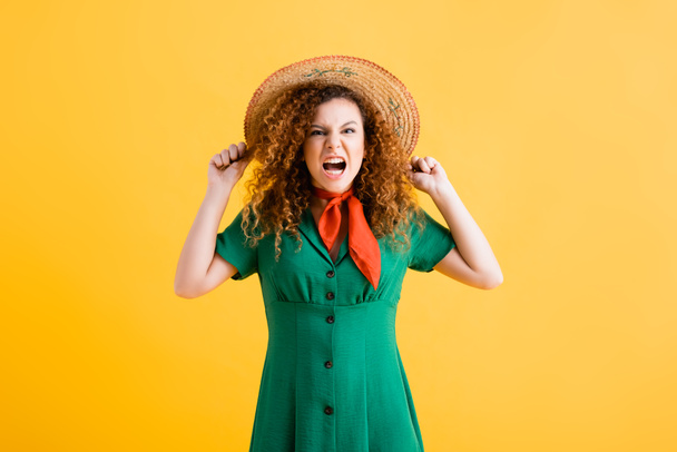 Wütende junge Frau mit Strohhut und grünem Kleid schreit auf gelb  - Foto, Bild