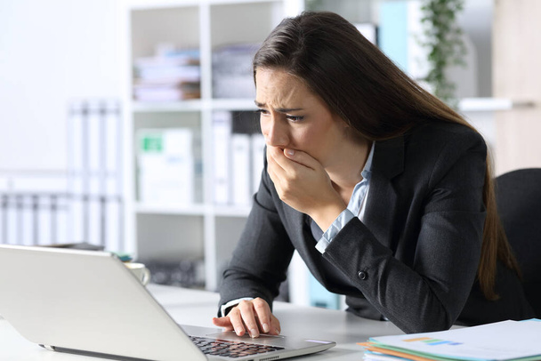 Sad executive woman reading bad news on laptop sitting on a desk at the office - 写真・画像