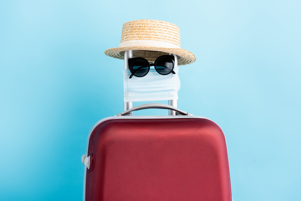 aurinkolasit, lääketieteellinen naamio ja olkihattu punaisissa matkatavaroissa sinisellä - Valokuva, kuva