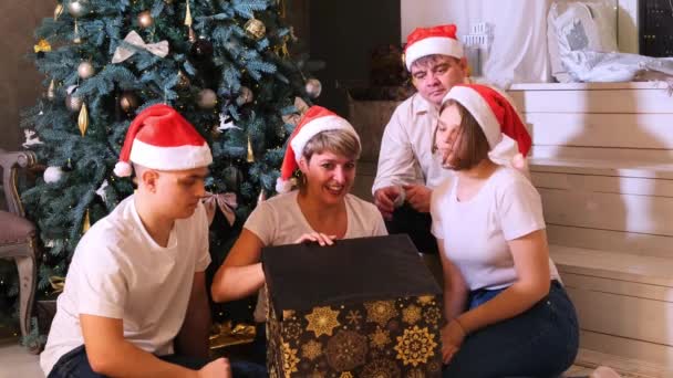 familie met kerstmutsen wisselt geschenken uit voor de kerstboom. - Video