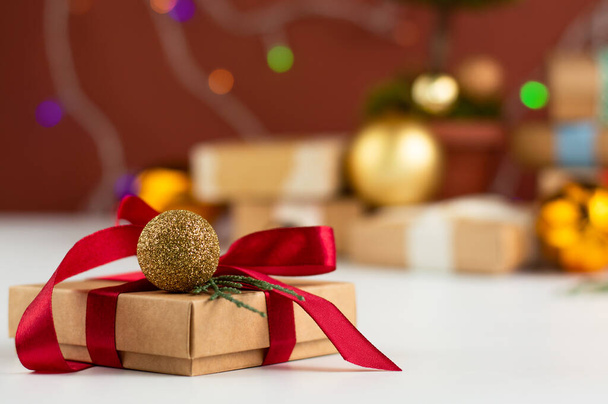 En primer plano es un regalo de Navidad bellamente decorado, en el fondo es una imagen borrosa de regalos y decoraciones navideñas. - Foto, Imagen