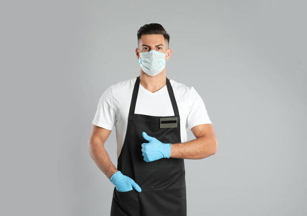 Waiter wearing medical face mask on light grey background - Φωτογραφία, εικόνα
