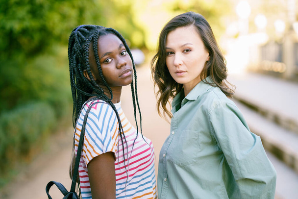 Dos jóvenes amigos mirando la cámara juntos en la calle. Mujeres multiétnicas. - Foto, Imagen
