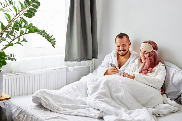 caucasian married couple have rest with smartphone on bed - Fotó, kép