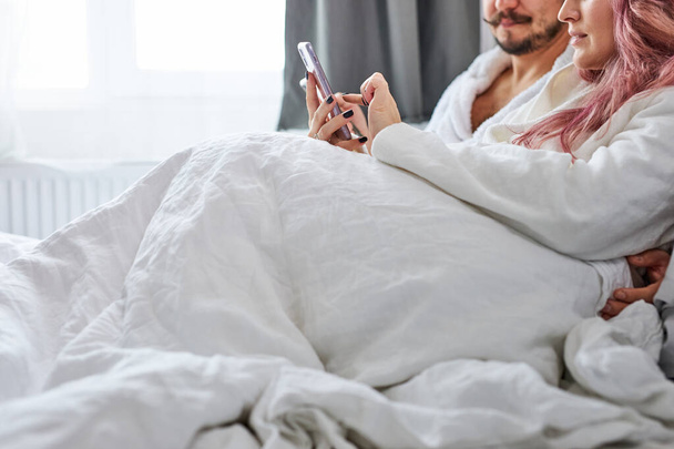 man and woman with smartphones in pajamas on their bed - Photo, image