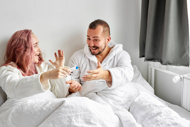 joyful couple finding out results of a pregnancy test at home lying on bed - Foto, afbeelding