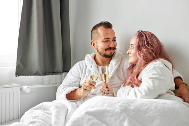 young couple caucasian man and woman wearing white housecoat, drinking sparkling wine - Foto, Imagem