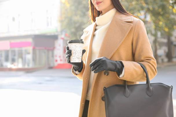 Woman with stylish leather gloves and cup of coffee on city street, closeup - Foto, Imagen