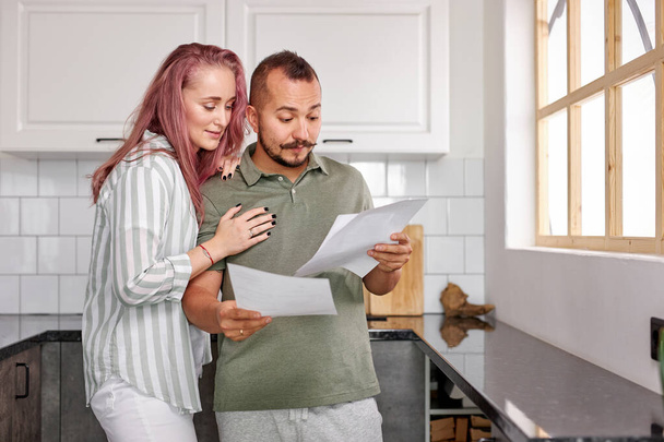 young caucasian couple checking bills documents in the kitchen - Foto, afbeelding