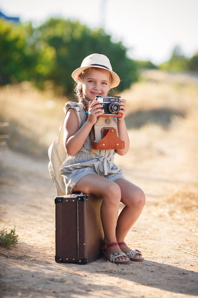 cestovatelka dětí. výlet sám. dívka kráčí s kamerou a kufr na přírodu po moři. cestování, dovolená, dovolená - Fotografie, Obrázek