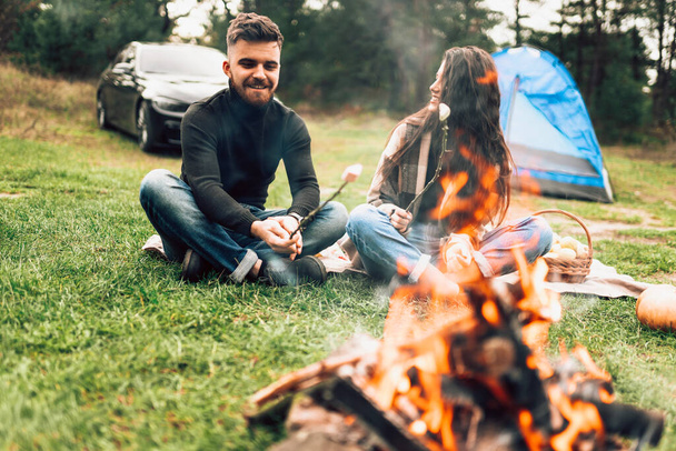 キャンプファイヤーの近くの自然の中でロマンチックなカップルは、マシュマロを焙煎 - 写真・画像