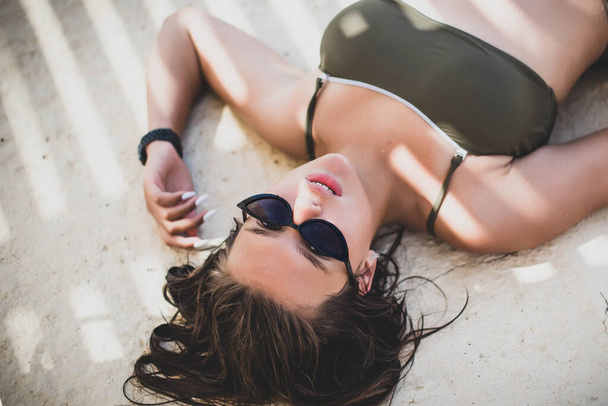 Fashion cute young teenage girl or woman posing lying in summer swimsuit . Trendy girl posing. Funny and positive woman in sunglasses - Foto, Imagen
