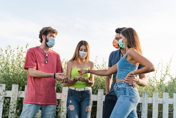 Gruppo di giovani che indossano una maschera protettiva usando gel igienizzante insieme contro la pandemia del coronavirus (covid-19) - Felice amicizia e nuovo concetto normale con i giovani che si divertono insieme - Foto, immagini