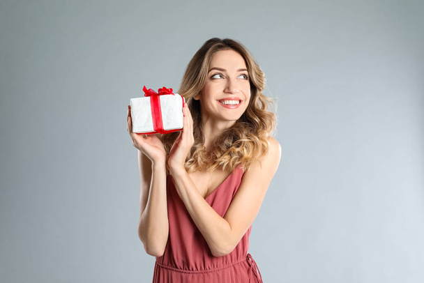 Beautiful young woman with Christmas present on light grey background - Fotó, kép