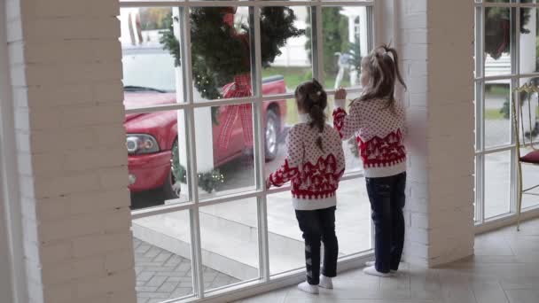 Μικρά παιδιά με ζεστά πουλόβερ και τζιν κοιτάζουν το αυτοκίνητο στο δρόμο κοντά στο σπίτι τους - Πλάνα, βίντεο