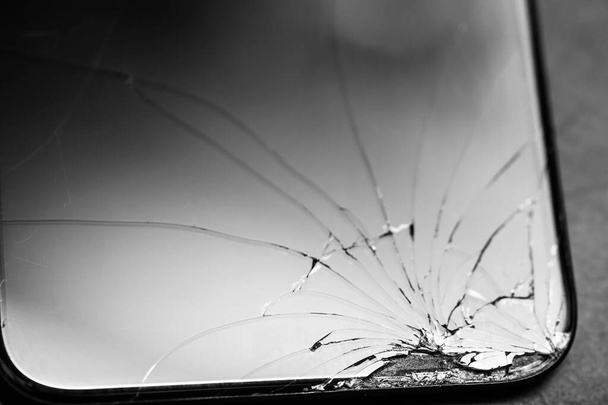 The cell phone screen is shattered. Web of cracks in all directions, black and white photo - Fotografie, Obrázek