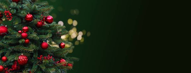 Closeup of Festively Decorated Outdoor Christmas tree with bright red balls on blurred sparkling fairy background. Defocused garland lights, Bokeh effect. High quality photo - Zdjęcie, obraz