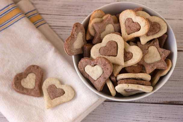 Shortbread cookies of two colors in a white plate on a wooden background. Sweet cookies in the form of hearts for February 14 (Valentine's Day) - Photo, Image