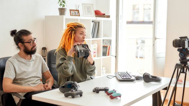 Woman with dreadlocks holding vr glasses. Young male and female technology blogger recording video blog or vlog about new gadgets at home - Valokuva, kuva